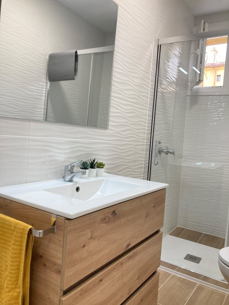 Baño 1 con mueble de madera, lavabo y ducha con mampara