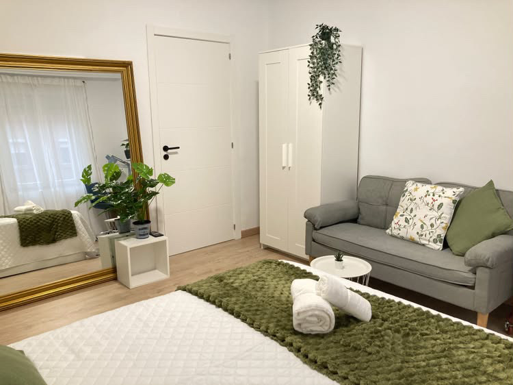 Habitación A con cama, sofá gris, armario y espejo de marco dorado
